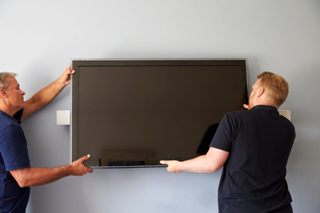 two men fitting flat screen television to wall